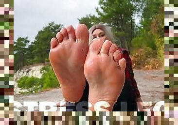 Mistress smears oil on her bare feet against the backdrop of the sea